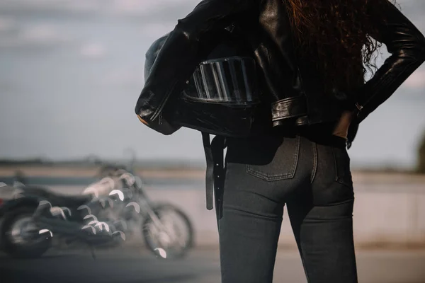 Vista ritagliata di donna in possesso di casco moto, moto in piedi su sfondo — Foto stock
