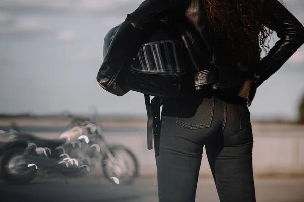 Vista recortada de la mujer sosteniendo casco de moto, moto de pie sobre el fondo - foto de stock