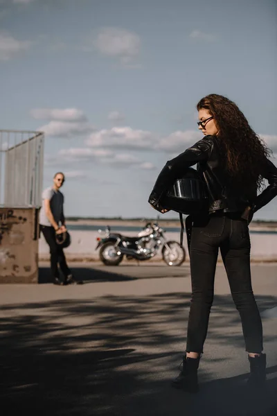 Chica sosteniendo casco y de pie delante de novio con moto - foto de stock