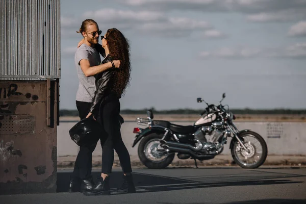 Jovens motociclistas abraçando na cidade com motocicleta clássica em segundo plano — Fotografia de Stock