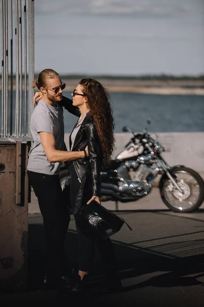 Jóvenes ciclistas abrazándose en la ciudad con moto vintage en el fondo - foto de stock