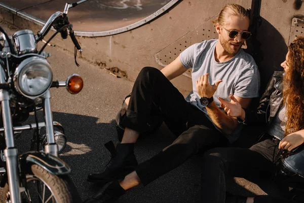 Couple talking and sitting on asphalt with classical motorbike — Stock Photo