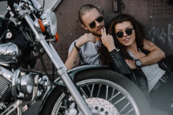 Couple hugging and smoking cigarette on asphalt with chopper motorbike — Stock Photo