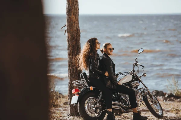 Couple in black leather jackets sitting on classical chopper motorbike on seashore — Stock Photo