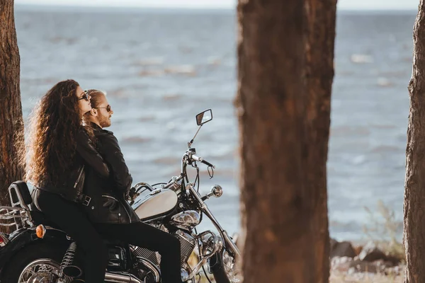 Casal de motociclistas em jaquetas de couro preto sentado na motocicleta e olhando para o mar — Fotografia de Stock