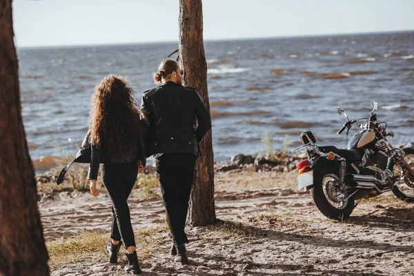 Vista posteriore della coppia che si tiene per mano e cammina sulla riva del mare, moto da crociera in piedi vicino — Foto stock