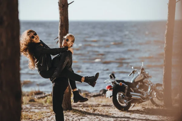 Copain avoir du plaisir et tenant sa petite amie sur les bras sur le bord de la mer avec moto près — Photo de stock