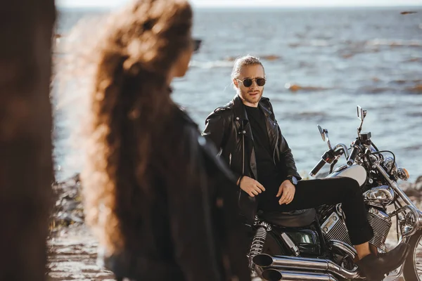 Foyer sélectif de fille regardant son petit ami assis sur la moto sur le bord de la mer — Photo de stock