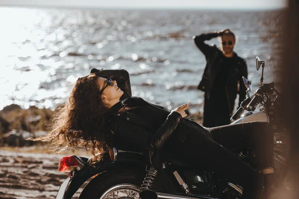 Foco seletivo de menina relaxante na motocicleta, enquanto namorado olhando para ela na praia — Fotografia de Stock