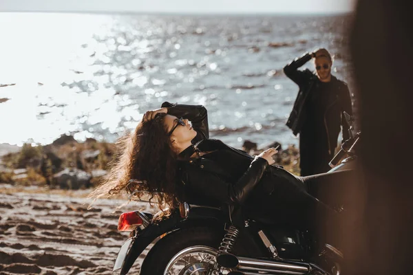 Selective focus of woman lying on motorbike while boyfriend looking at her on seashore — Stock Photo