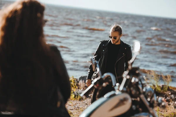 Foyer sélectif de la femme assise sur la moto et regardant petit ami marchant sur le bord de la mer — Photo de stock