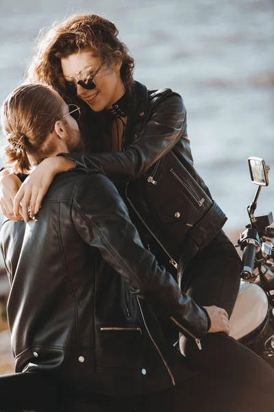 Couple de motards en cuir noir vestes câlins sur la moto sur le bord de la mer — Photo de stock