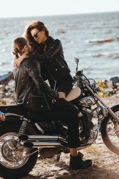 Pareja de ciclistas abrazándose en motocicleta clásica en la orilla del mar - foto de stock