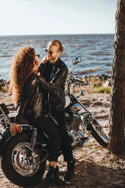 Pareja de ciclistas abrazando en motocicleta clásica en la orilla del mar - foto de stock