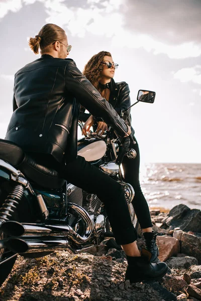 Par de motociclistas em jaquetas de couro preto com helicóptero motocicleta perto do mar — Fotografia de Stock