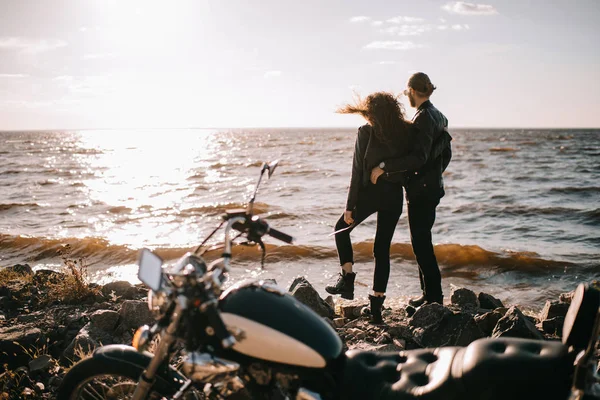 Selektiver Fokus des Paares bei Sonnenuntergang über dem Meer und Motorrad im Vordergrund — Stockfoto