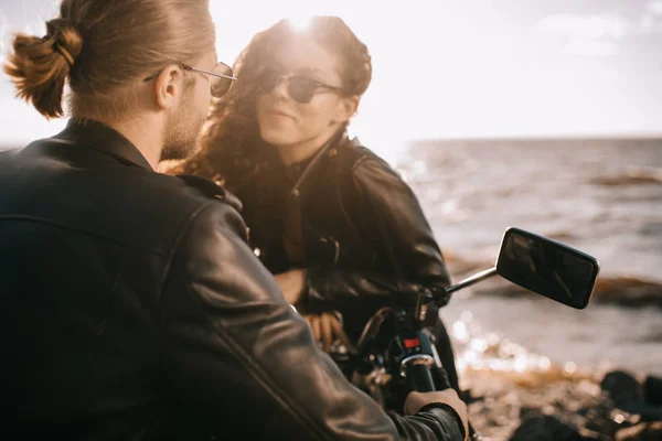 Girl flirting with biker while he sitting on motorcycle near sea with back light — Stock Photo