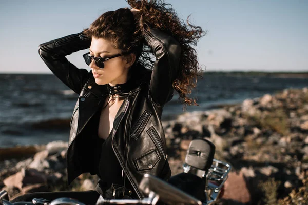 Hermosa chica rizada en gafas de sol sentado en la motocicleta - foto de stock