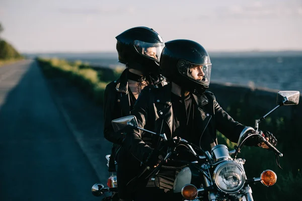 Pareja de ciclistas en cascos a caballo motocicleta clásica en la carretera del campo - foto de stock