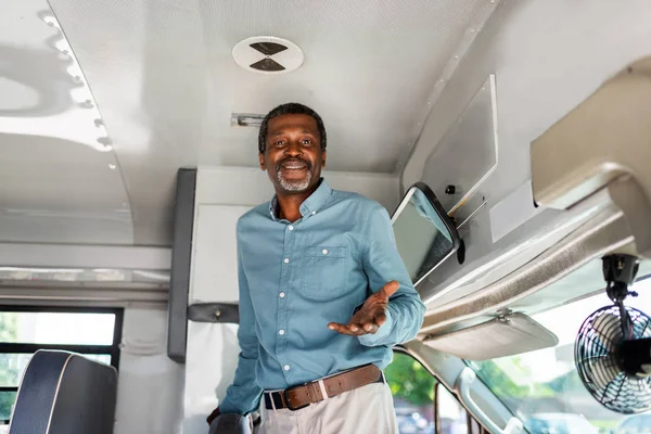 Happy mature african american bus driver standing inside bus and looking at camera — Stock Photo