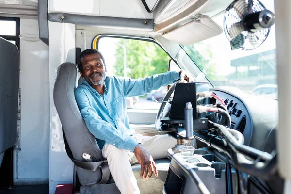 Усміхнений зрілий афроамериканський водій автобуса дивиться на камеру, сидячи всередині автобуса — стокове фото