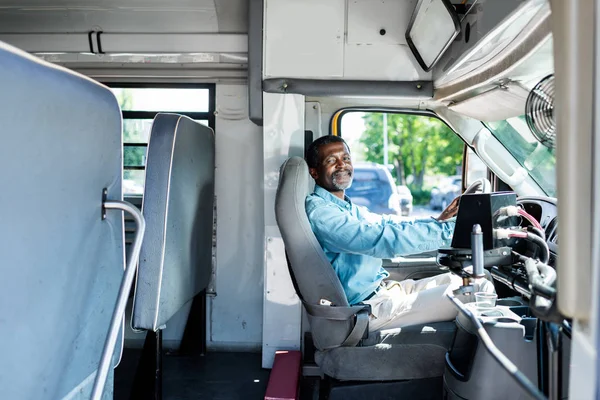 Mature pilote afro-américain assis à bus et regardant la caméra — Photo de stock