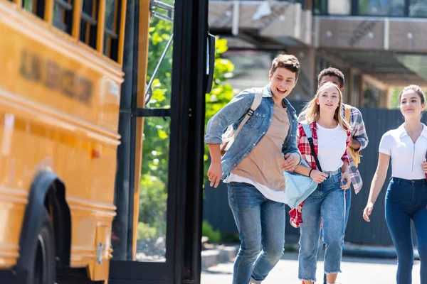 Group of happy teen scholars running to school bus after lessons to get home — Stock Photo