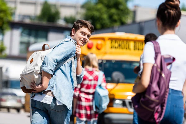Задний вид улыбающегося школьника, идущего в школьный автобус со своими одноклассниками и поворачивающегося назад — стоковое фото