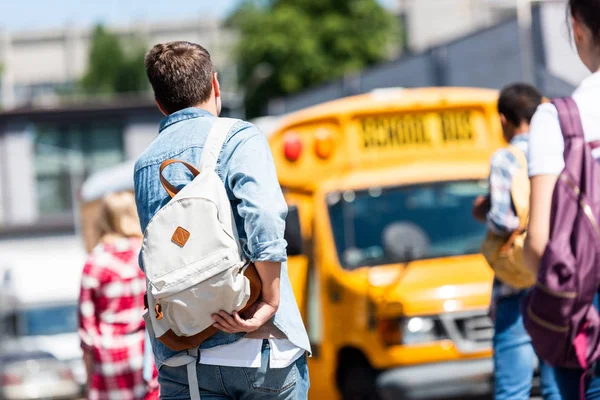 Vista trasera del grupo de estudiantes adolescentes con mochilas caminando al autobús escolar después de la escuela - foto de stock