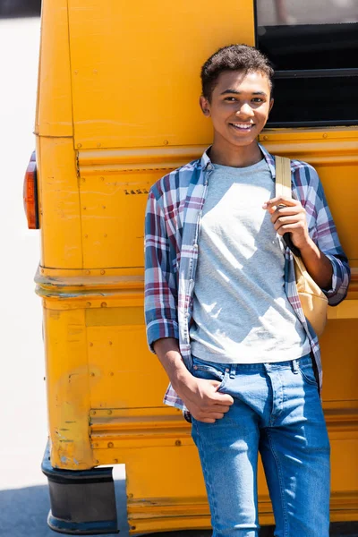 Happy teen african american schoolboy leaning back on school bus — Stock Photo