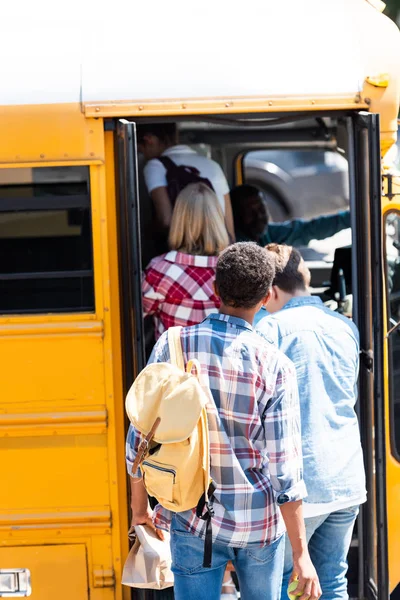 Rear view of teen classmates walking into school bus — Stock Photo