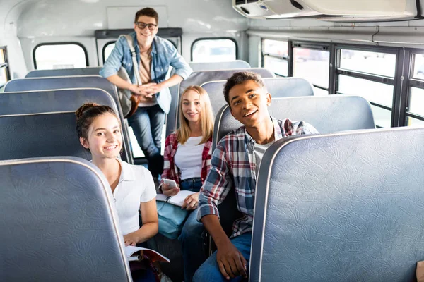 Grupo de estudiantes adolescentes felices montando autobús escolar y mirando a la cámara - foto de stock