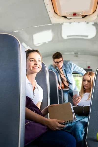 Feliz adolescente colegiala cabalgando autobús escolar con compañeros de clase y mirando hacia otro lado - foto de stock