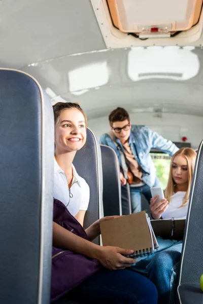 Adolescente feliz estudante equitação ônibus escolar com colegas de classe e olhando para longe — Fotografia de Stock