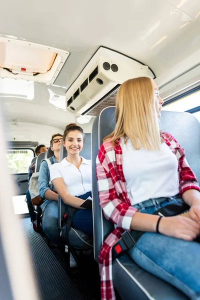 Happy teen schoolgirl riding school bus with classmates and looking at camera — Stock Photo