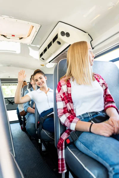 Adolescente feliz estudante equitação ônibus escolar com colegas de classe e acenando para a câmera — Fotografia de Stock