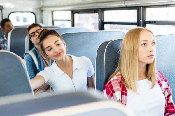 Felice teen studentessa equitazione scuolabus con compagni di classe e in attesa su strada — Foto stock