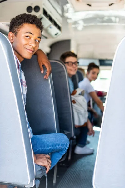 Happy teen students sitting at school bus and looking back at camera — Stock Photo