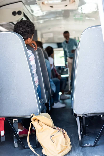 Задний вид подростков, сидящих в школьном автобусе и слушающих учителя — стоковое фото