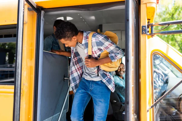 Estudiante afroamericano caminando fuera del autobús escolar - foto de stock