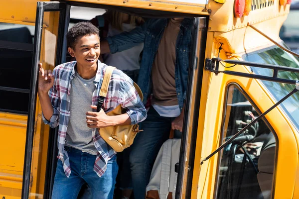 Africano americano feliz estudiante caminando fuera de escolar autobús con compañeros de clase - foto de stock