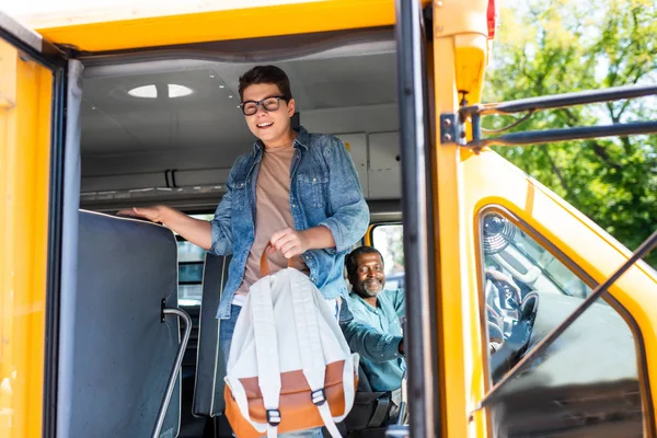 Happy teen schoolboy walking out of school bus while driver looking at him — Stock Photo
