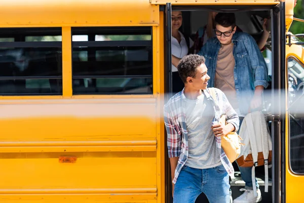 Grupo de adolescentes eruditos caminando fuera del autobús escolar - foto de stock
