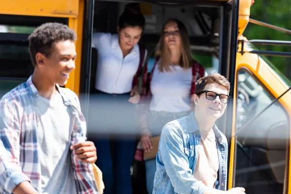 Grupo de estudiantes felices adolescentes caminando fuera del autobús escolar - foto de stock