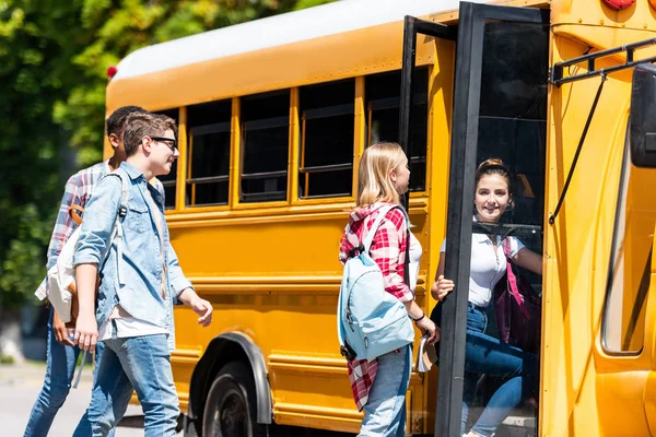 Grupo de jóvenes eruditos felices entrando en el autobús escolar después de clases - foto de stock