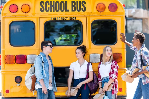 Група підлітків-вчених спілкується, спираючись на шкільний автобус — стокове фото