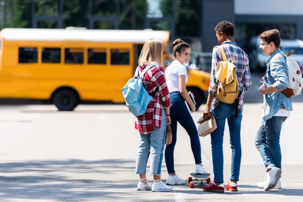 Grupo de adolescentes eruditos pasar tiempo juntos en el estacionamiento frente al autobús escolar - foto de stock