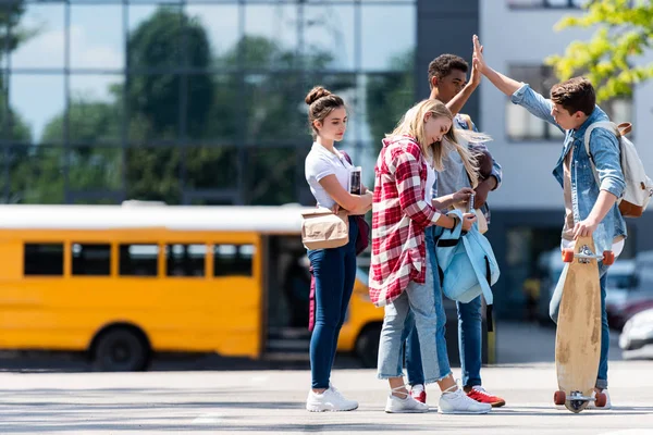 Grupo de estudiantes adolescentes que dan cinco en el estacionamiento frente al autobús escolar - foto de stock