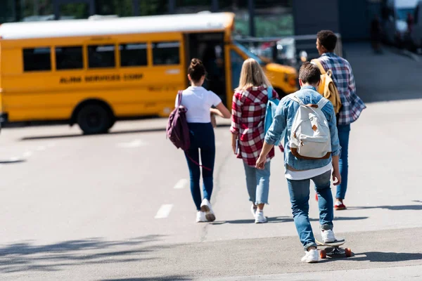 Rückansicht einer Gruppe von Teenagern, die auf dem Parkplatz zum Schulbus laufen — Stockfoto