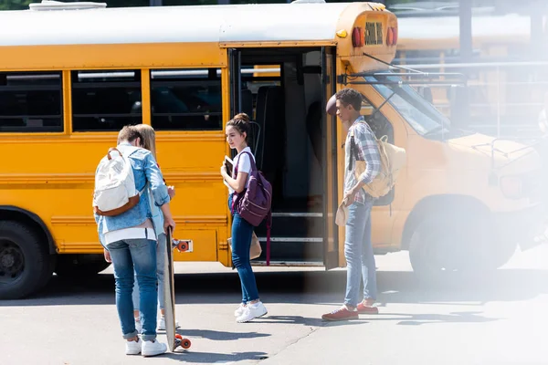 Grupo de adolescentes eruditos de pie cerca de autobús escolar - foto de stock